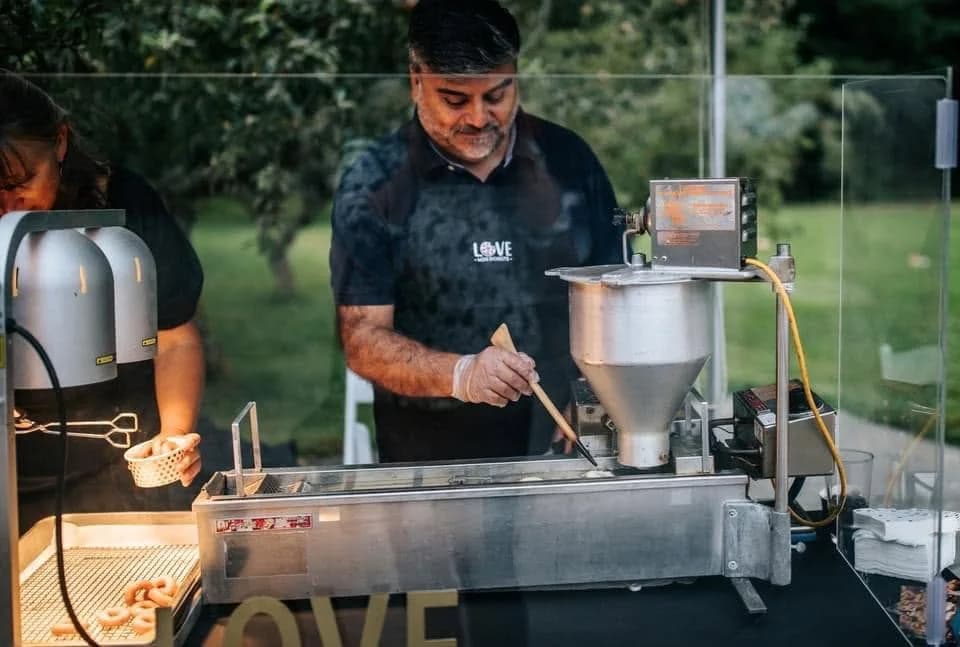 Turning mini donuts in the fryer under the tent at an evening event.